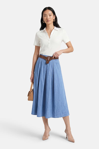 Jupe 3/4 bleu clair en denim de Terra di Siena avec une ceinture marron et un chemisier blanc.
