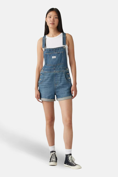 Denim combishort in middieblauw van Levi's, gedragen over een witte tanktop en hoge sneakers.