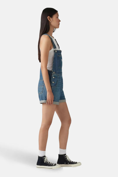 Combi-short en denim bleu moyen de Levi's, porté avec un débardeur blanc et des baskets montantes noires.