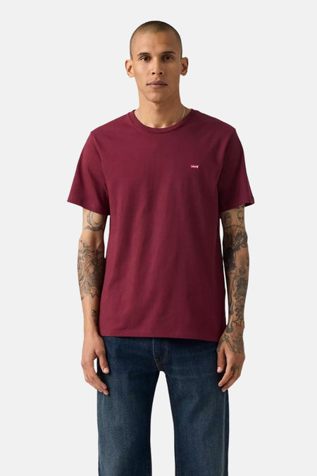 T-shirt bordeaux à manches courtes de Levi's, porté avec un jean bleu, homme aux bras tatoués.