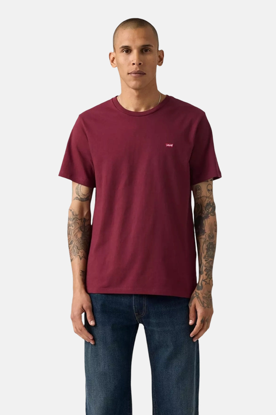 Bordeaux T-shirt met korte mouwen van Levi's, gedragen met een blauwe spijkerbroek, man met getatoeëerde armen.