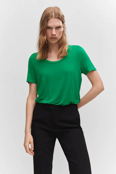 Green short-sleeve top with rounded neckline, worn by model in lifestyle pose, paired with black trousers