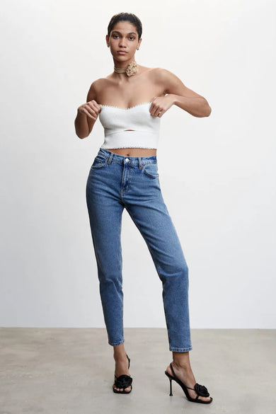Blauwe 'Mom'-jeans van MANGO, gedragen met een witte top en schoenen met hakken versierd met een zwarte bloem.