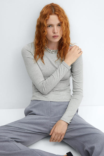 Grijze trui met lange mouwen van MANGO, gedragen met een zilveren ketting en een grijze broek.