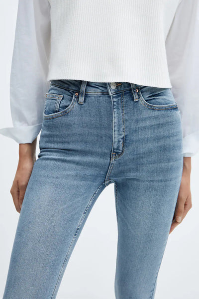 Light blue skinny jeans with faded wash and classic five-pocket design, worn with a white ribbed top, front cropped view