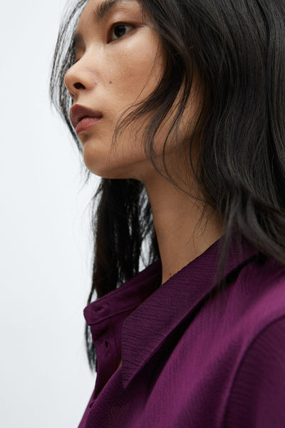 Mauve long-sleeve blouse with textured fabric and classic collar, side view close-up of model with dark hair