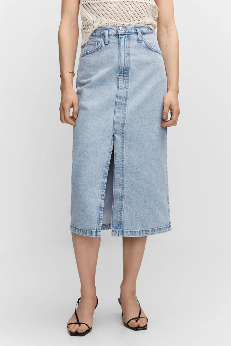 Light blue denim midi skirt with front slit and classic five-pocket design, worn with a white knit top and black sandals, front view.