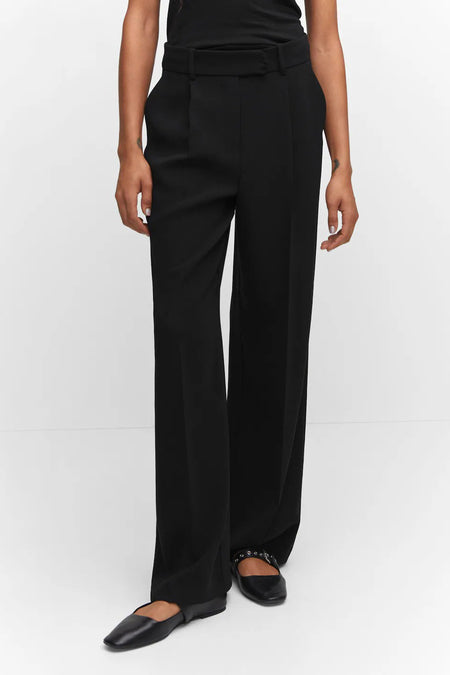 Black wide-leg dress pants with front pleats and belt, worn with black top and flat shoes, full-length front view