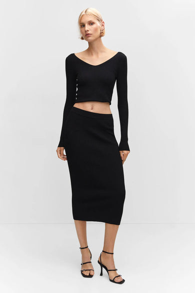 Black ribbed midi skirt by [brand omitted] with high waist, form-fitting silhouette, worn with black long-sleeve top and strappy heels, full-length front view