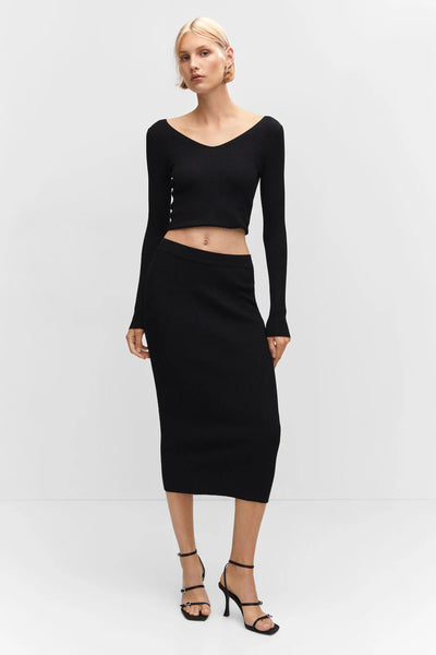 Black ribbed midi skirt by [brand omitted] with high waist, form-fitting silhouette, worn with black long-sleeve top and strappy heels, full-length front view