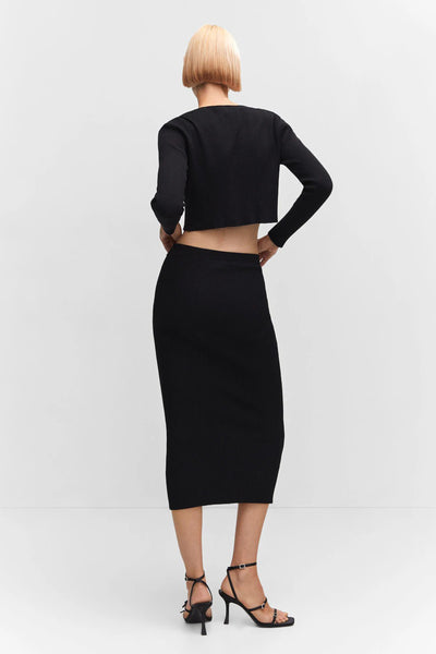 Black ribbed midi skirt from back view, fitted silhouette with high waist, worn with cropped top and strappy heels