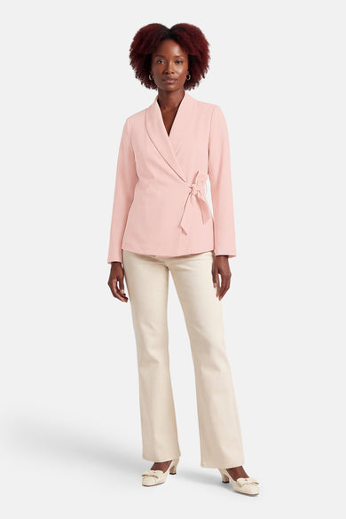 Blazer rose de Terra di Siena, avec une ceinture à nouer et porté avec un pantalon et des escarpins crème.
