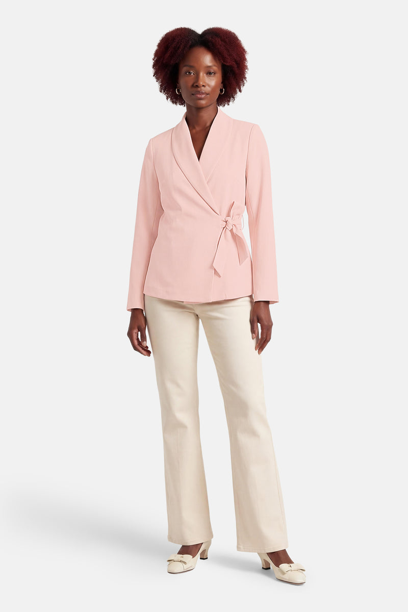 Blazer rose de Terra di Siena, avec une ceinture à nouer et porté avec un pantalon et des escarpins crème.
