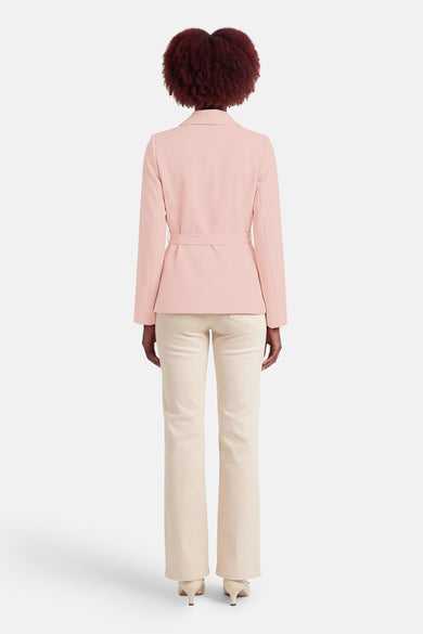 Blazer rose, de Terra di Siena, avec une ceinture ton sur ton, porté sur un pantalon crème.
