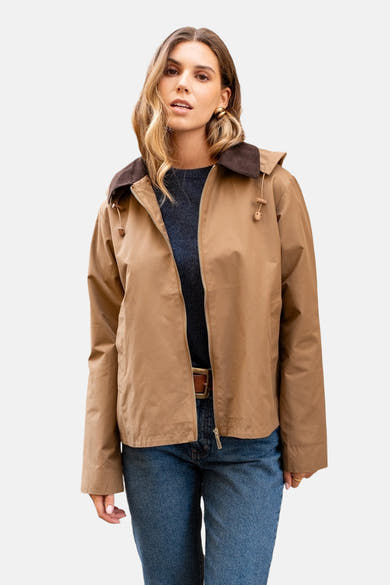 Veste de pluie cognac de LAURA JO, avec capuche et col en velours côtelé marron, portée avec un pull bleu marine et un jean.
