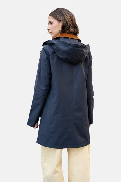 Marineblauwe regenjas van LAURA JO, met capuchon en bruine voering, gedragen met een beige broek.