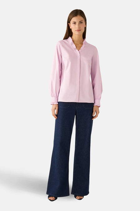 Blouse rose à manches longues de MORE & MORE, avec volants au col et aux poignets, portée avec un jean large.
