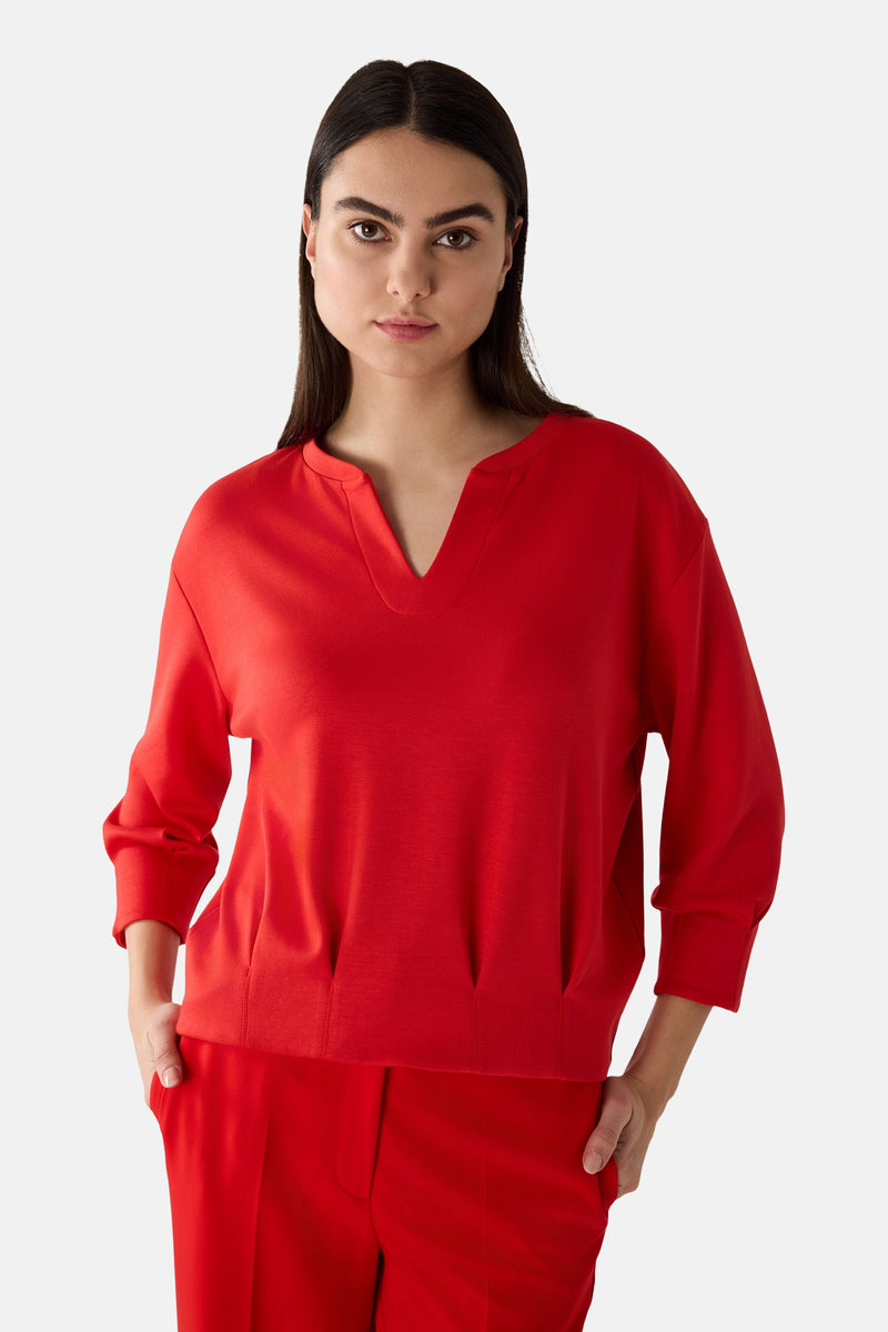 Rode V-hals sweatshirt van MORE & MORE, gedragen met een bijpassende broek en beige sneakers.