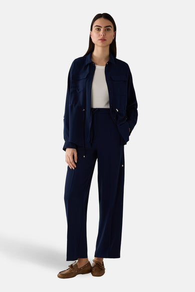 Gilet bleu de MORE & MORE avec poches, boutons et cordon coulissant, porté sur un t-shirt blanc et un pantalon assorti.