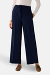 Pantalon de costume bleu de MORE & MORE, coupe ample avec ceinture à nouer, porté avec un haut blanc et des chaussures bateau.

