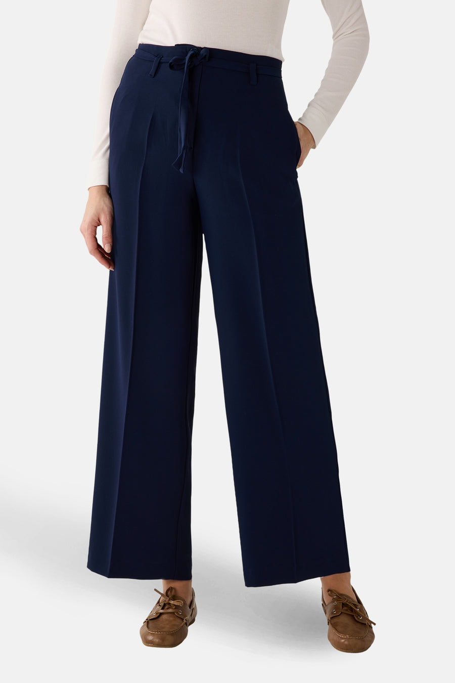 Pantalon de costume bleu de MORE & MORE, coupe ample avec ceinture à nouer, porté avec un haut blanc et des chaussures bateau.
