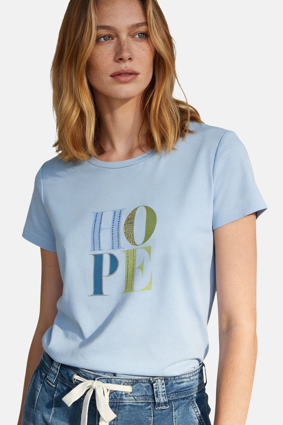 Blauw T-shirt met korte mouwen van MORE & MORE, versierd met het decoratieve woord 'HOPE' en gedragen met een spijkerbroek.