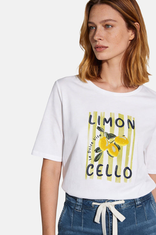 T-shirt blanc à manches courtes de MORE & MORE, imprimé avec des citrons sur rayures, porté avec un pantalon bleu.
