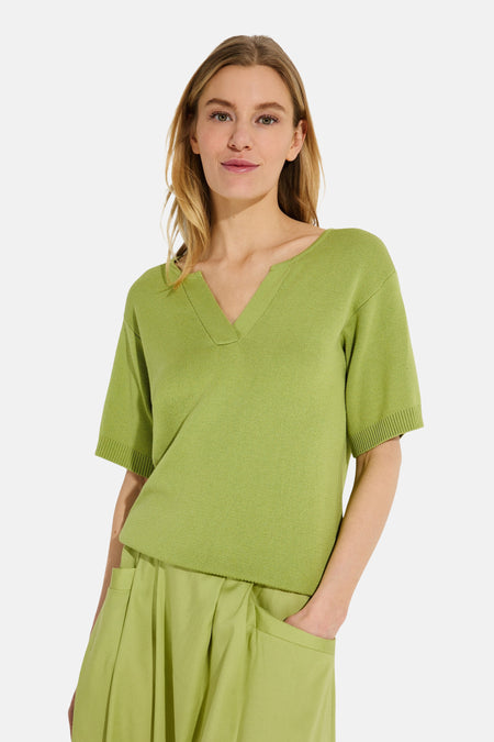 Groene V-hals trui van MORE & MORE, gedragen met een bijpassende geplooide lange rok en sandalen met hak.