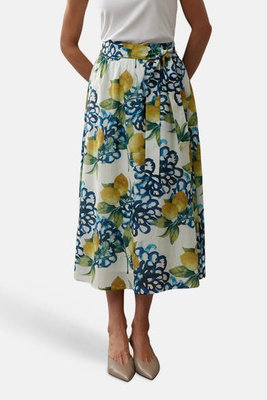 Multikleurige lange rok van MORE & MORE, bloemen- en citroenprint, gedragen met een wit T-shirt en beige sandalen met hak.