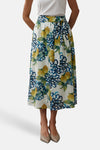 Multikleurige lange rok van MORE & MORE, bloemen- en citroenprint, gedragen met een wit T-shirt en beige sandalen met hak.
