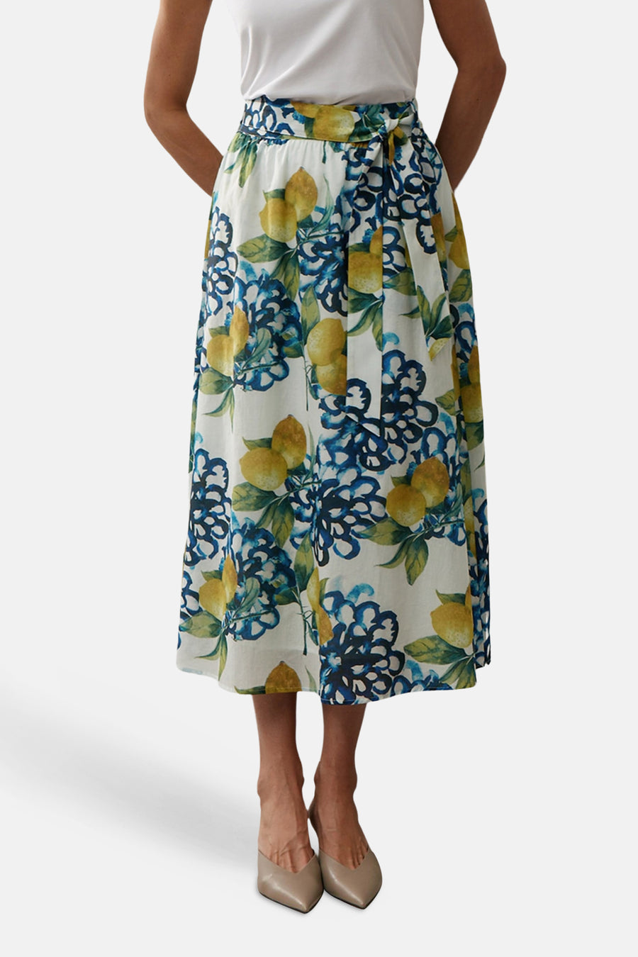 Multikleurige lange rok van MORE & MORE, bloemen- en citroenprint, gedragen met een wit T-shirt en beige sandalen met hak.
