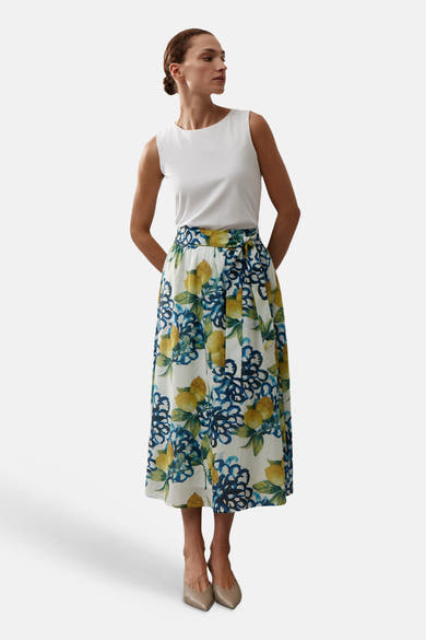 Jupe longue multicolore de More & More, à motif citron et floral bleu, portée avec un haut blanc et des chaussures nude.