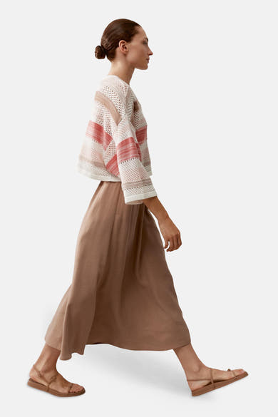 Pull col rond multicolore de MORE & MORE à mailles ajourées et rayures horizontales, porté avec une jupe beige et des sandales.