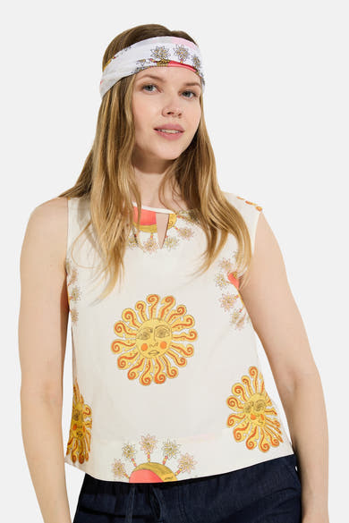 Crèmekleurig mouwloos hemd van het merk MORE & MORE, versierd met veelkleurige motieven van zon, maan en bloemen, met een knoop aan de achterkant.