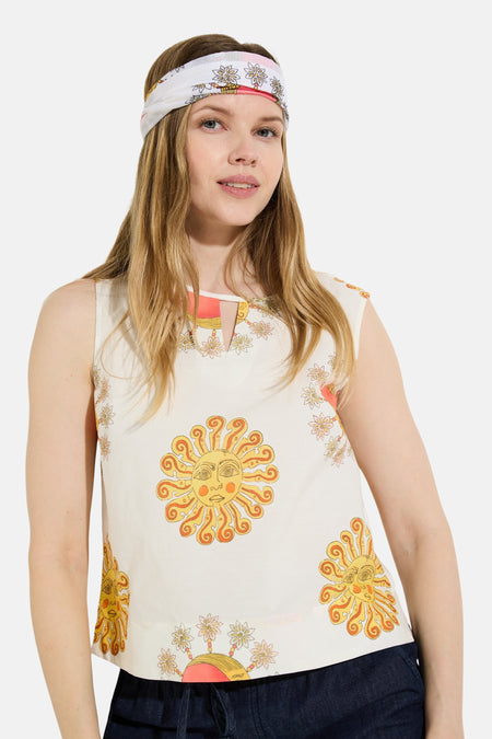 Crèmekleurig mouwloos hemd van het merk MORE & MORE, versierd met veelkleurige motieven van zon, maan en bloemen, met een knoop aan de achterkant.