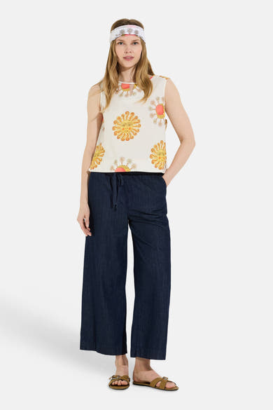 Blouse sans manches multicolore de MORE & MORE, à motifs de soleils jaunes et fleurs roses, portée avec un jean large et un bandeau assorti.