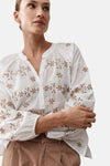 Wit blouse van MORE & MORE met bruine bloemenborduursels, wijde lange mouwen, gedragen met een bruine broek en muiltjes.