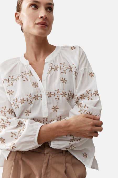 Wit blouse van MORE & MORE met bruine bloemenborduursels, wijde lange mouwen, gedragen met een bruine broek en muiltjes.