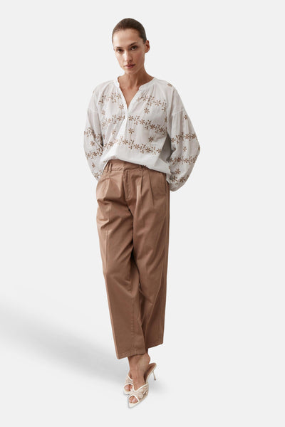 Blouse blanche de MORE & MORE à broderies florales marron, manches longues amples, portée avec un pantalon marron et des mules.