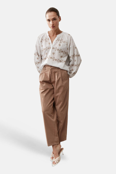 Blouse blanche de MORE & MORE à broderies florales marron, manches longues amples, portée avec un pantalon marron et des mules.