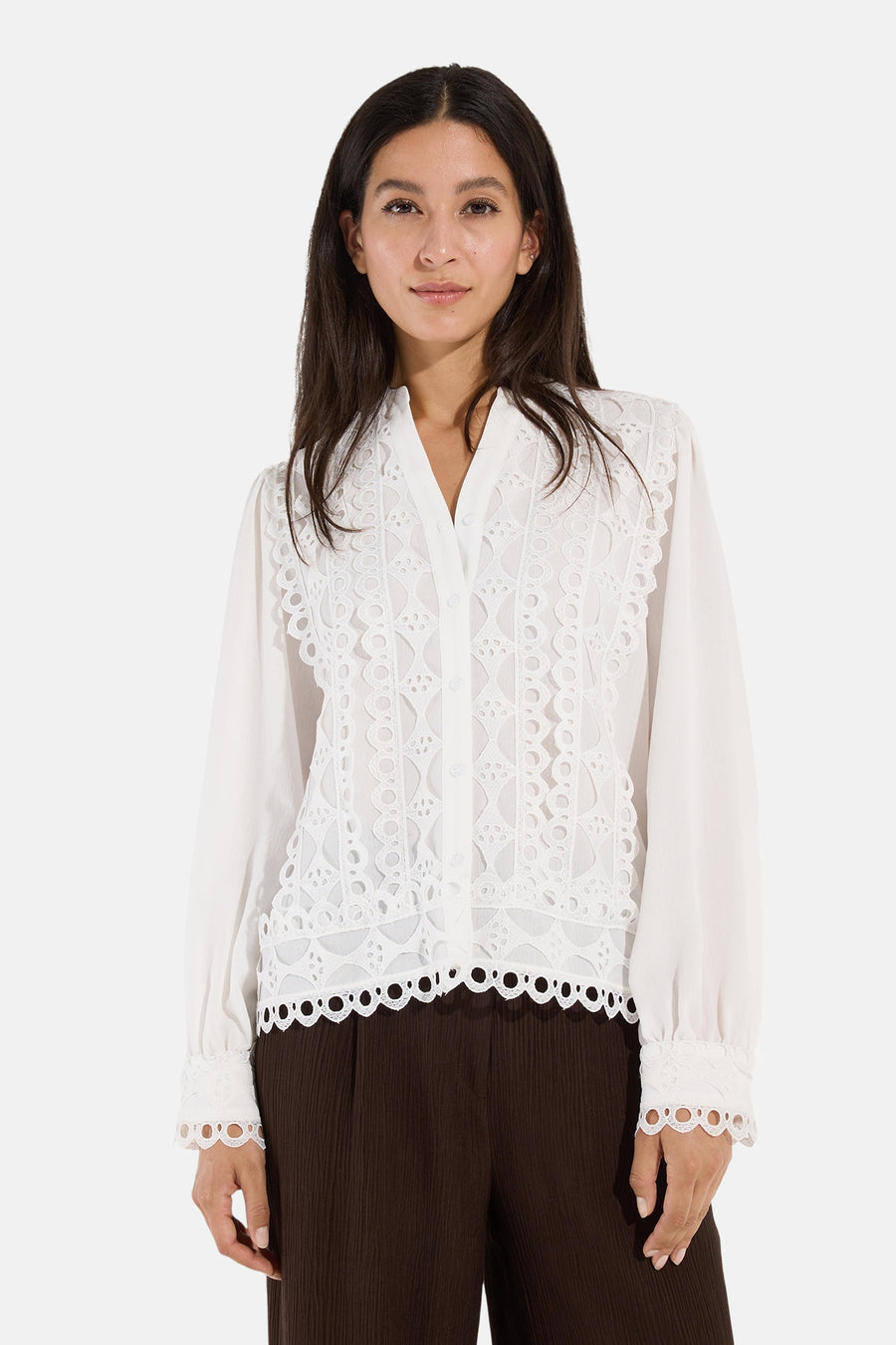 White long-sleeve blouse with lace detailing by MORE & MORE, featuring scalloped edges and button front, worn with brown ribbed pants.