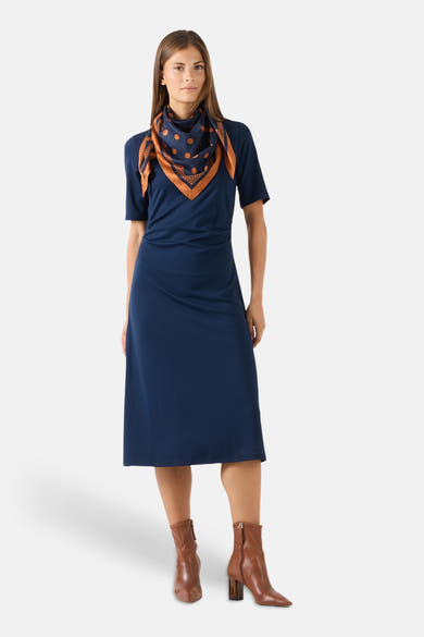 Multicolored silk foulard with navy base and orange polka dots by MORE & MORE, styled as neck scarf on model in navy dress and brown boots, front view.