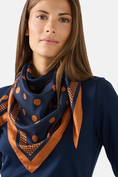 Multicolored silk foulard with navy base and orange polka dots, by MORE & MORE, styled in a draped neck wrap on model wearing navy top.