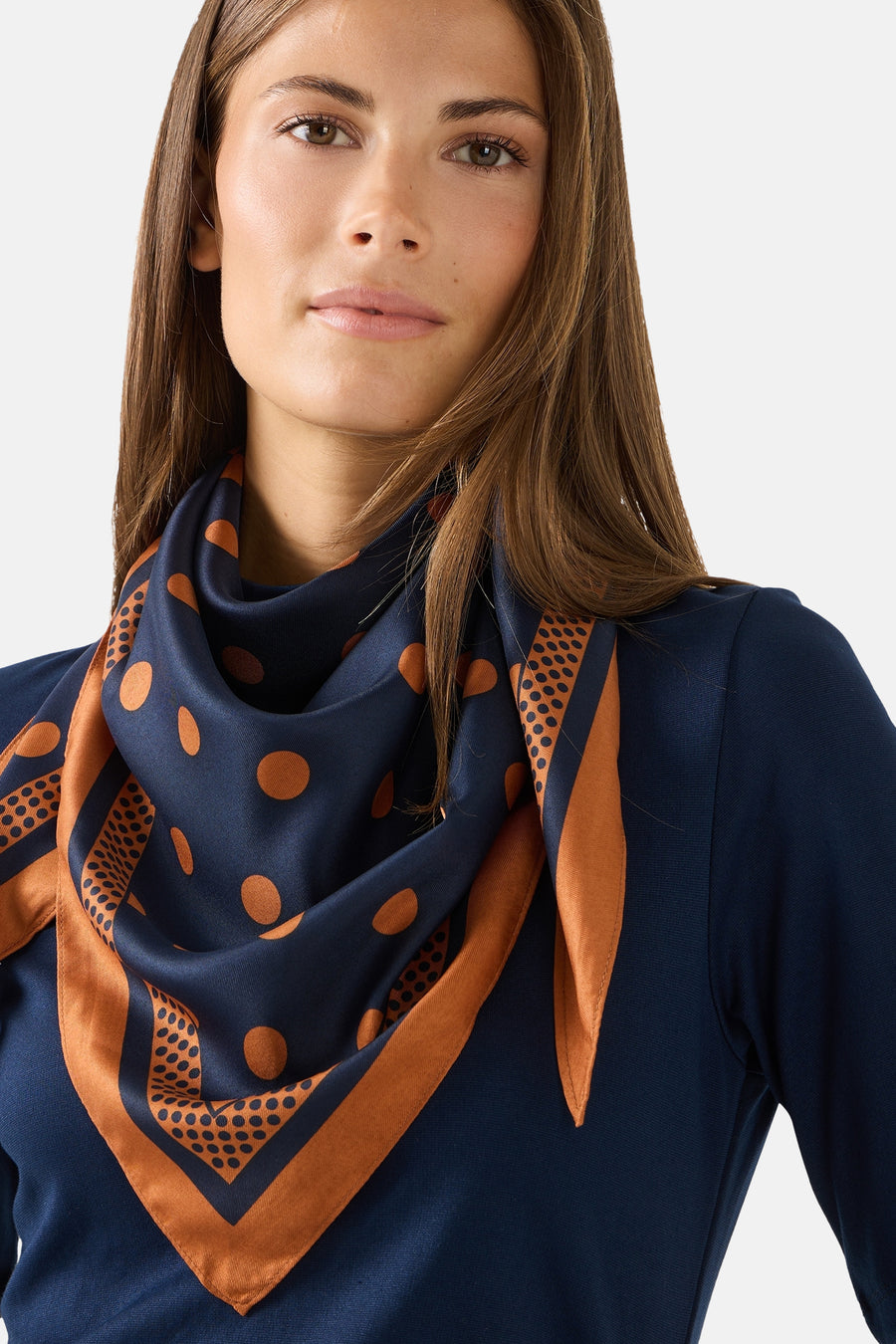 Multicolored silk foulard with navy base and orange polka dots, by MORE & MORE, styled in a draped neck wrap on model wearing navy top.