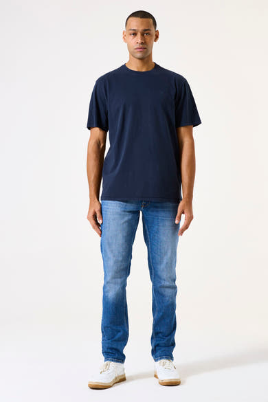 Middelblauwe, nauwsluitende jeans van GARCIA, gedragen met een effen marineblauw T-shirt en witte sneakers.