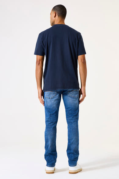 Garcia middentoon blauwe tapered jeans, gedragen met een marineblauw T-shirt en witte sneakers, van achteren gezien.