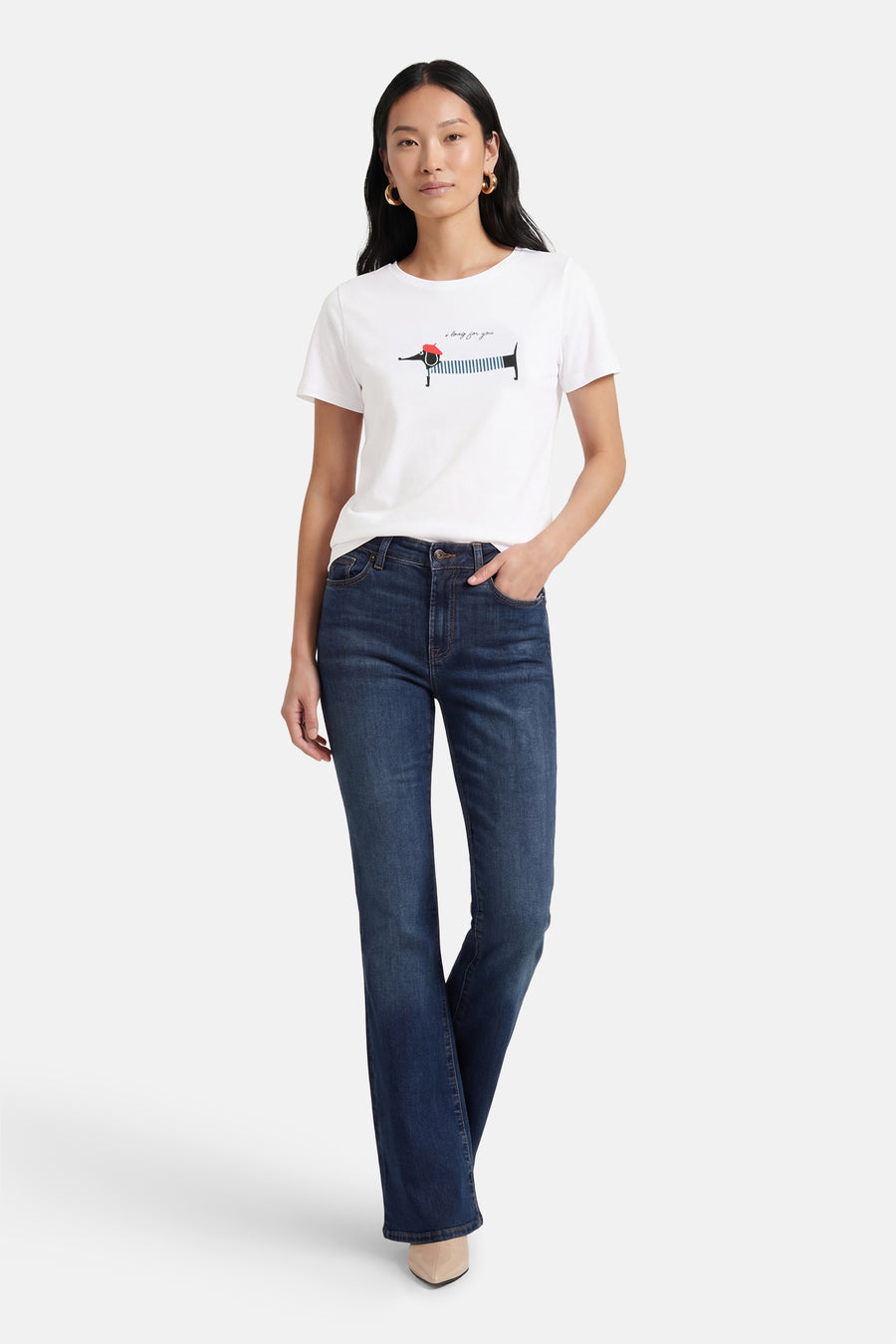T-shirt à manches courtes blanc de MORE & MORE, orné d'un motif teckel, porté avec un jean bleu et des escarpins beiges.
