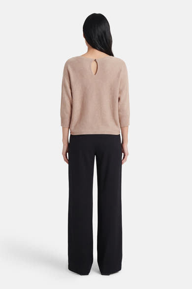 Pull à col rond beige de MORE & MORE, avec découpe goutte d'eau au dos, porté avec un pantalon noir.