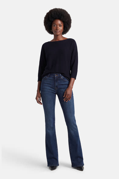 Pull à col rond bleu de MORE & MORE, porté avec un jean bootcut bleu foncé et des escarpins noirs pointus.