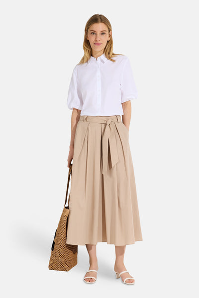 White short-sleeve button-down blouse with classic collar and relaxed fit, worn with beige pleated skirt and woven tote bag, front view.